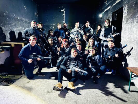 Grupa pracowników podczas emocjonującej gry Laser Tag na imprezie integracyjnej. Uczestnicy z replikami karabinów G36C poruszają się w wojskowym bunkrze, wykorzystując osłony i strategię zespołową. Dynamiczna akcja, skupienie na twarzach i duch rywalizacji sprawiają, że wydarzenie jest pełne adrenaliny i świetnej zabawy.